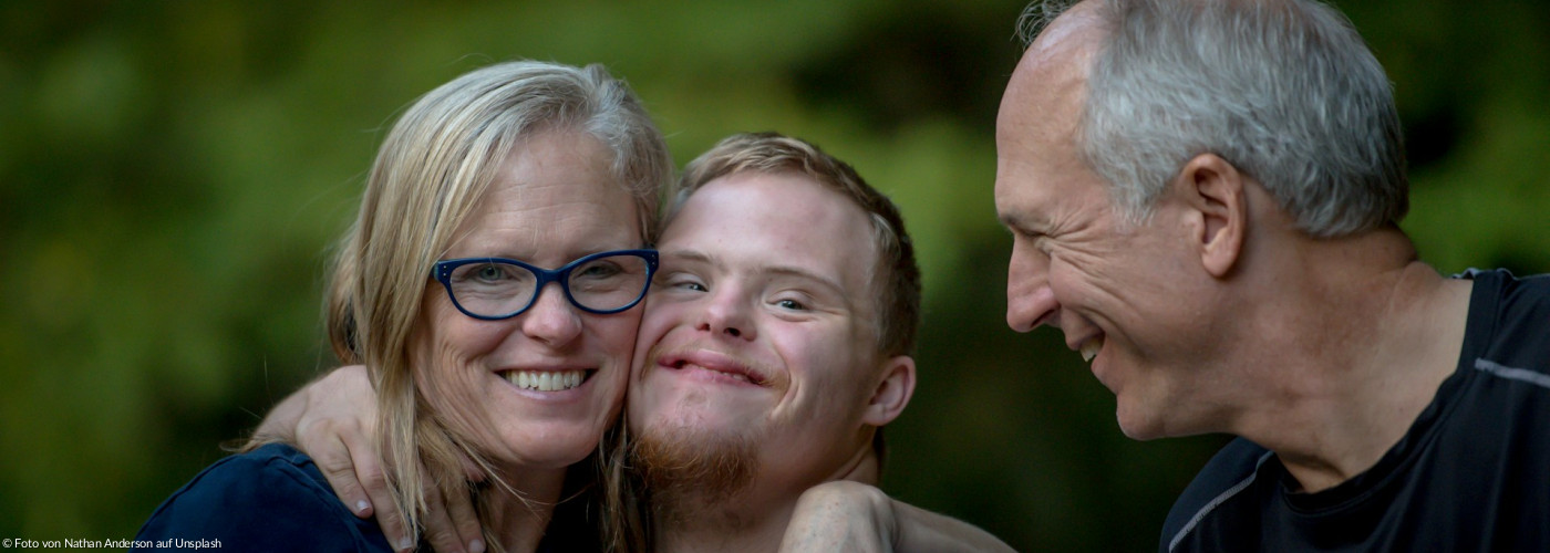 Foto von einer behinderten Person, die von einer Frau und einem Mann umarmt wird