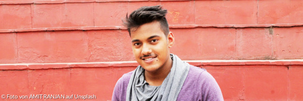 Pereson in lila Hemd und blauer Jeans sitzt auf Betonbank