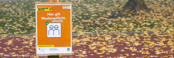 Braune Holzbeschilderung mit Aufschrift: "Hier gilt Maskenpflicht"