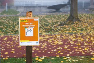 Braune Holzbeschilderung mit Aufschrift: "Hier gilt Maskenpflicht"